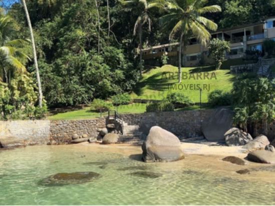 Fachada da casa vista da praia, entre coqueiros e rochas naturais