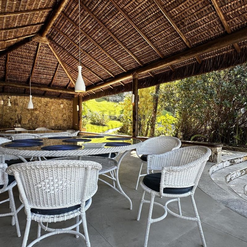 Área gourmet coberta com mesas e cadeiras, vista para o jardim