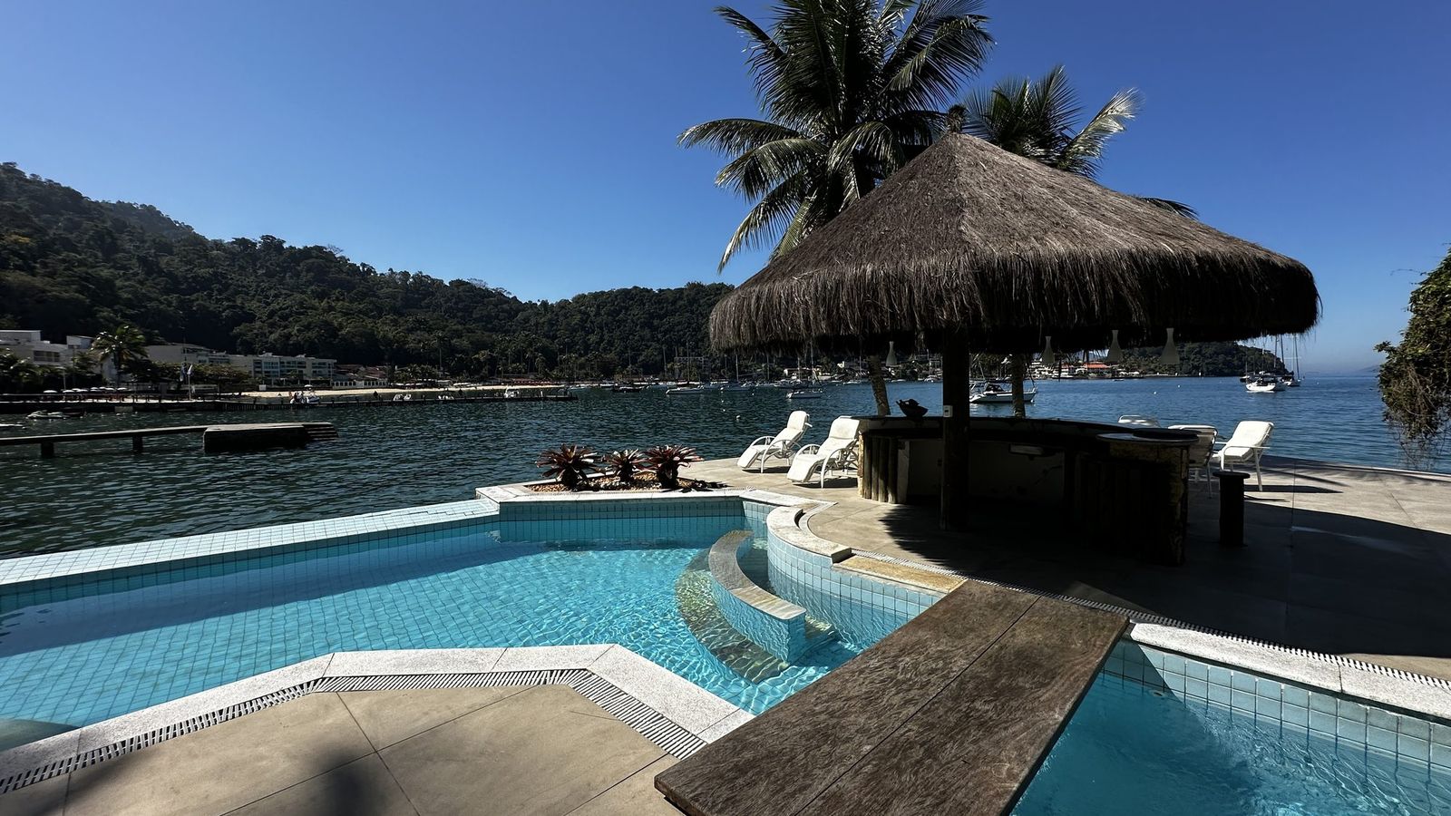 Piscina de borda infinita integrada ao mar, com quiosque de palha e espreguiçadeiras